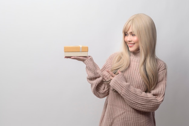 Portrait of Caucasian young woman wearing sweater holding gifts box over white background