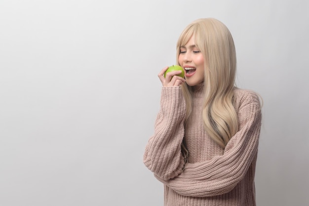 Portrait of Caucasian young woman wearing sweater holding green apple over white background