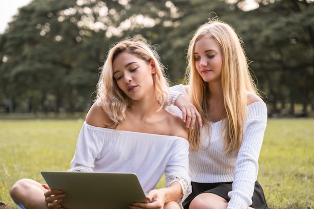 幸せと一緒にコンピューターのラップトップを使用して屋外の公園に座っている白人の若い女性の肖像画