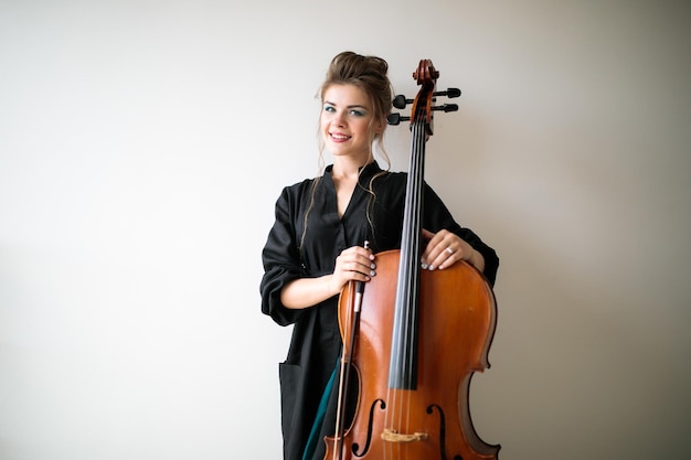 Portrait of a cellist girl on a light background a woman stands with a cello on a light background