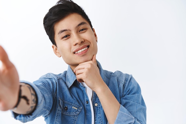 Portrait of charismatic smiling attractive asian man taking selfie on mobile phone trying make sassy thoughtful look hold smartphone and touch chin grinning happy white background