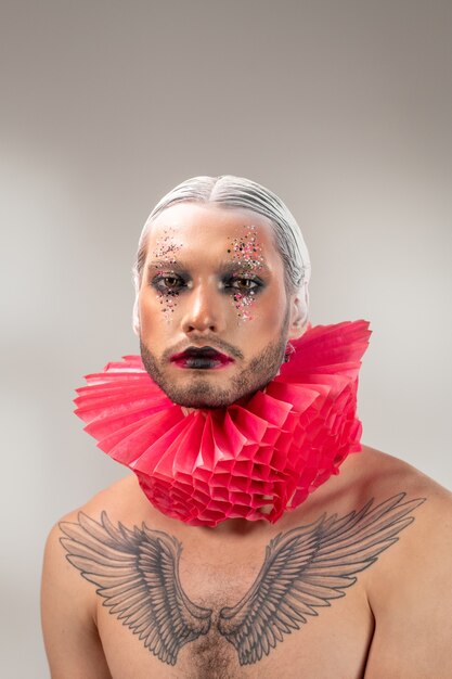 Portrait of charismatic young bearded man with white hair and bright dramatic makeup wearing red ruff against isolated background, he playing sad man