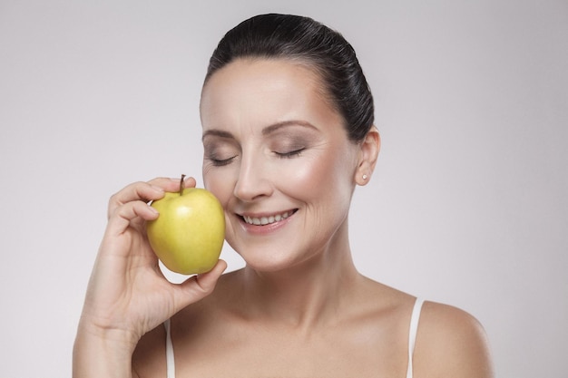 Portrait of charming beautiful healthy caucasian middle aged woman holding green apple, she love to eat fruit, make her get good health, nice skin, lose weight and weight control. Copy space, indoor