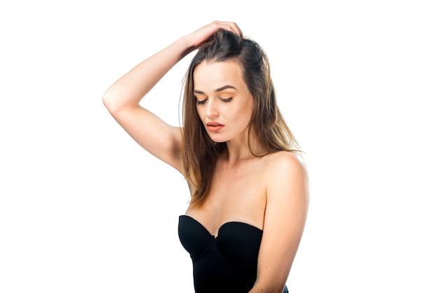 Portrait of charming beautiful woman in deep neckline dress. Girl with closed eyes holds hand near head. White background. Pretty female with closed eyes in black lingerie.