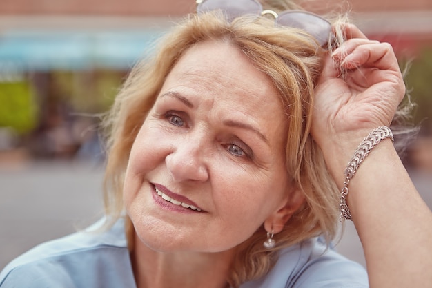 Portrait of charming Caucasian senior lady about 60 years old with blond hair and sunglasses.