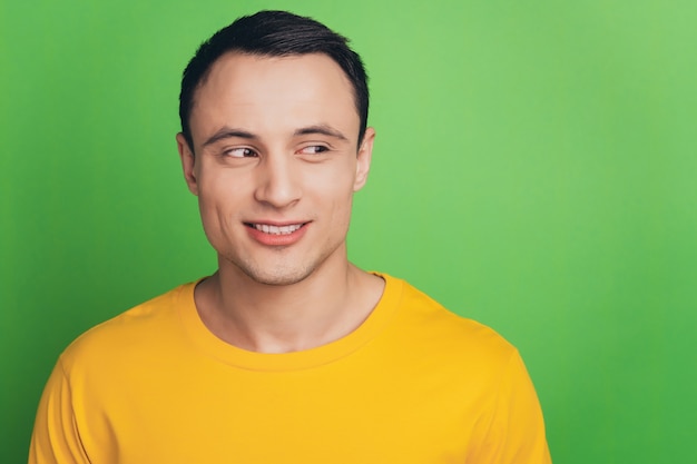 Portrait of charming cheerful guy toothy beaming smile look side blank space on green background