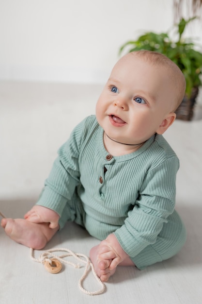 portrait of a charming chubby baby in a green jumpsuit sitting on the floor top view
