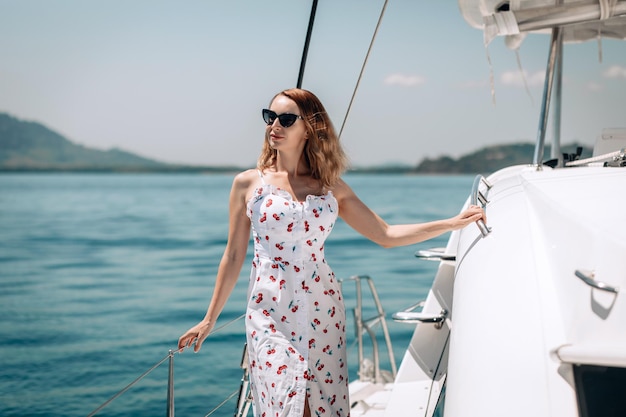 Portrait of a charming cute girl in a long white dress and sunglasses posing on a white yacht. Holiday vacation