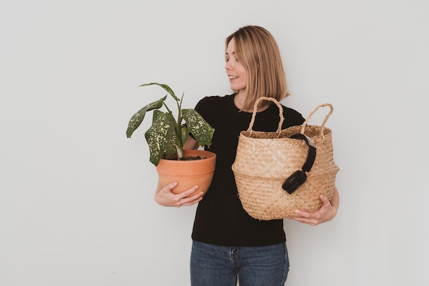 Portrait of charming European woman in casual clothes holding basket with things, flower in pot. Moving, garage sale or shopping concept On white background
