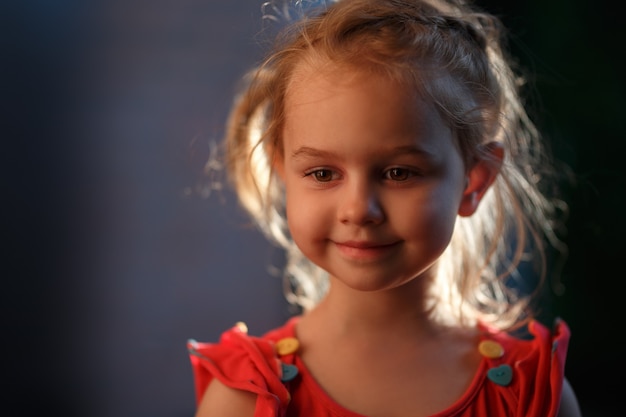 Portrait of a charming fair-haired girl standing outside on a warm summer evening, the sun illuminates the hair from behind.