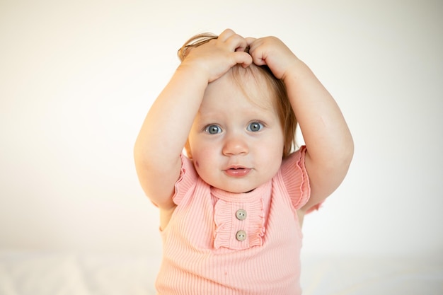 Portrait of a charming funny redhaired baby girl with blue eyes and a birthmark on her cheek Hemangioma Light background Lifestyle