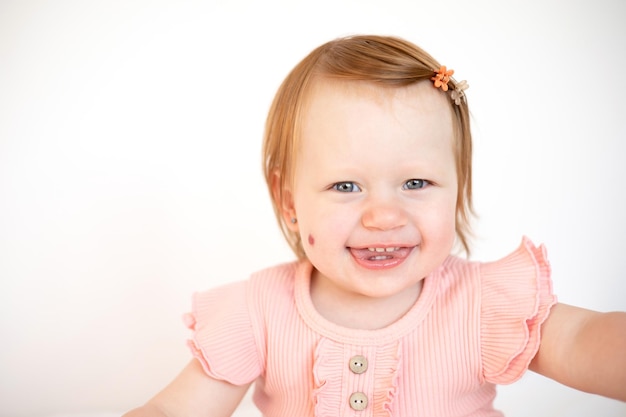 Foto ritratto di un'affascinante bambina dai capelli rossi con gli occhi azzurri e una voglia sulla guancia emangioma sfondo chiaro stile di vita