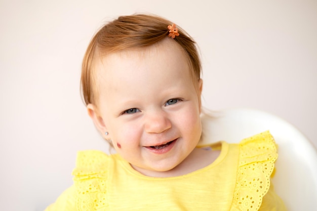 Portrait of a charming funny redhaired baby girl with blue eyes and a birthmark on her cheek Hemangioma Light background Lifestyle