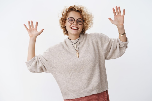 Photo portrait of charming and joyful charismatic blond woman in glasses and stylish warm sweater raising palms high and showing number ten describing something pleased.