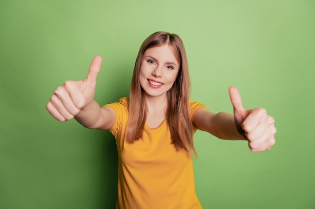 Portrait of charming lady show two thumbs up symbols wear yellow t-shirt isolated on green color background