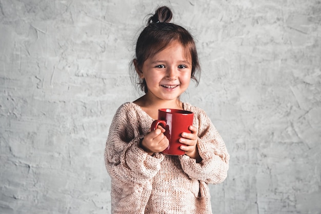Портрет очаровательной маленькой девочки в бежевом свитере на сером фоне