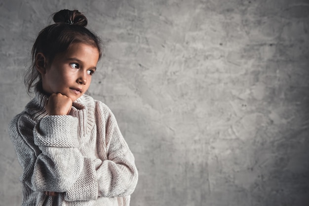회색 배경에 베이지색 스웨터를 입은 매력적인 어린 소녀의 초상화