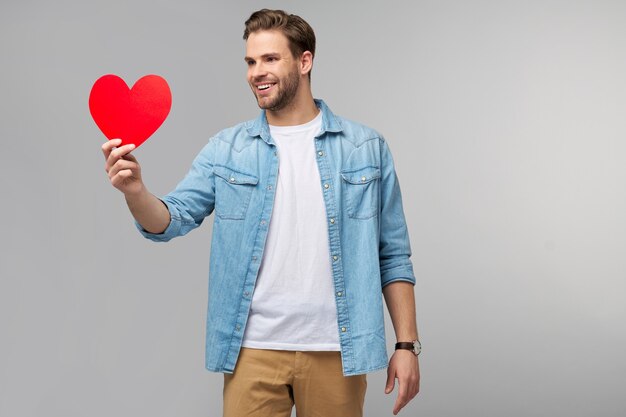 Portrait of charming man hold hand paper heart shaped card wear casual style shirt isolated over grey wall