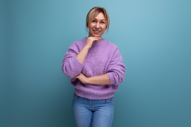 Portrait of a charming pleasant blond young woman in a purple sweater on a blue background with copy