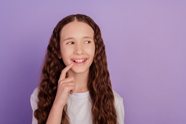 Portrait of charming pre-teen girl thinking touching finger chin isolated over violet background