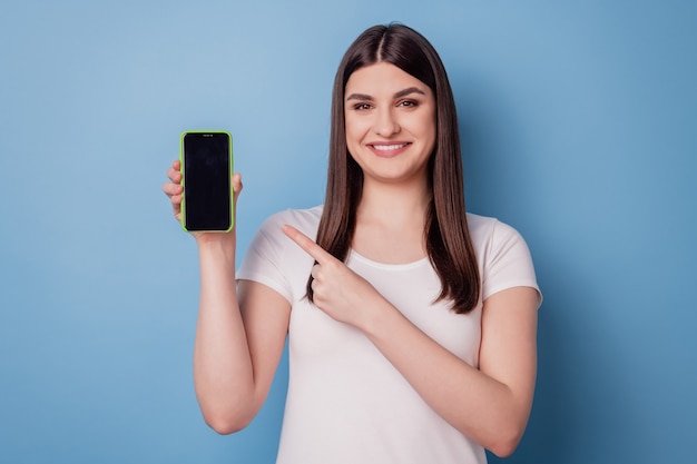 Portrait of charming promoter lady hold smartphone direct finger touchscreen show empty space on blue background