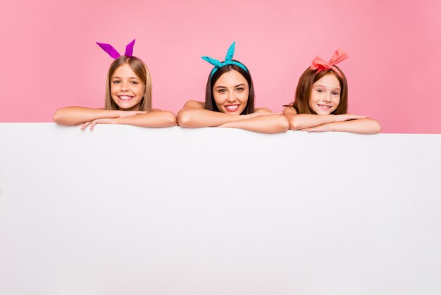 Portrait of charming three siblings with bright headbands putting hands on pattern isolated over pink background