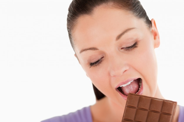 Portrait of a charming woman eating a chocolate block while standing