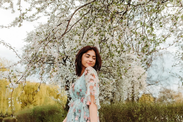 Portrait of charming woman posing near apple cherry tree blossoms blooming flowers in the garden