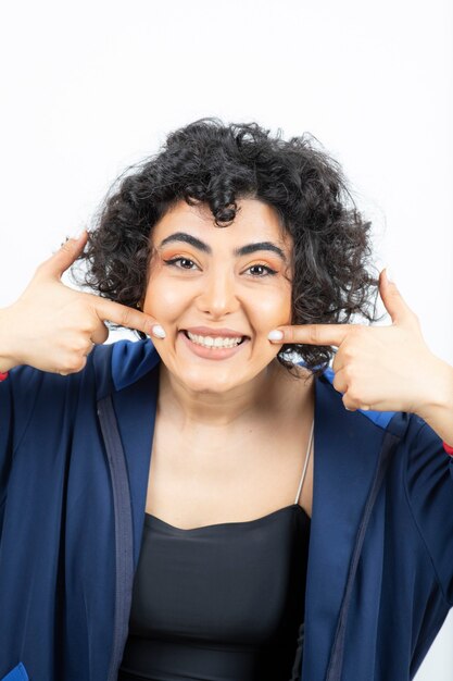 Portrait of a charming woman with curly hair pointing at her toothy smile .