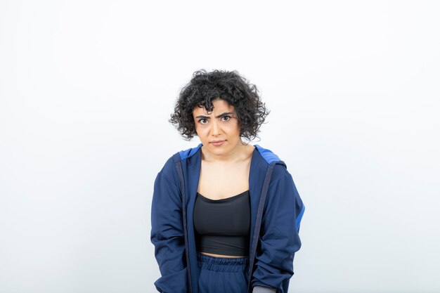 Portrait of a charming woman with curly hair posing against white wall .