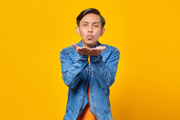 Portrait of charming young asian man holding palms sending air kiss to girlfriend