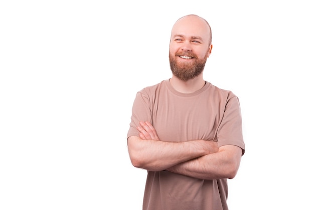 Portrait of charming young bearded man looking away with crossed arms over white wall