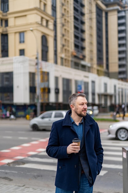 Portrait of a charming young businessman dressed in suit and coat. Standing outside a modern building.