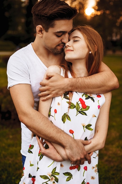 デート中にキスする前に目を閉じて夕日に対して官能的な抱擁を抱く魅力的な若いカップルの肖像画。