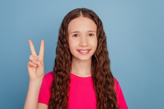 Portrait of charming young little lady demonstrate v-sign on blue background