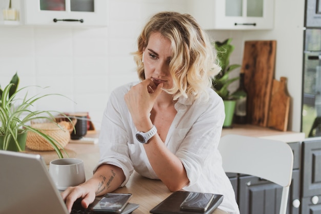 Portrait of charming young woman in headphones with laptop working at home in the kitchen