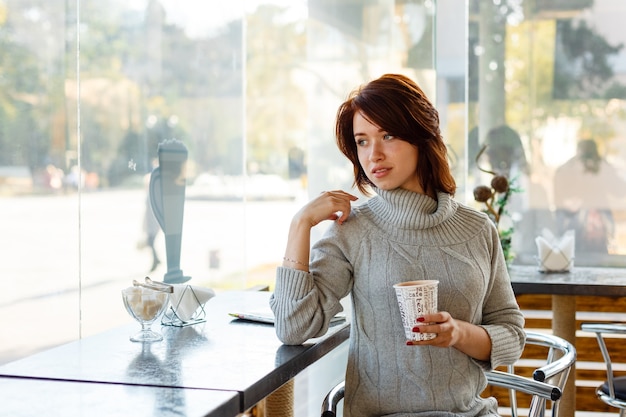 Portrait of charming young woman with friendly smile brunette in a knitted sweater smiling at wi