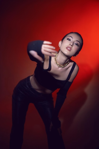 Портрет дерзкой сексуальной красивой молодой девушки в черной одежде стоит в студии на красном фоне
