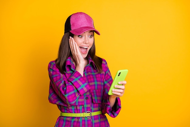 Portrait of cheerful addicted person look phone arm on cheek plaid violet outfit hat isolated on yellow color background