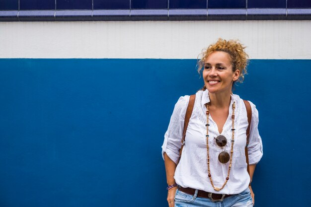 Portrait of cheerful adult blonde woman and blue and white wall in scene