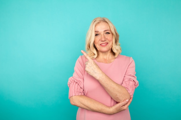 Portrait of cheerful adult woman pointing something in the blue wall.