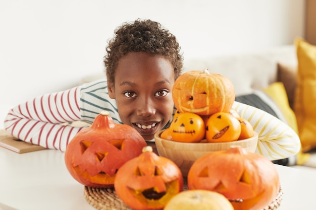 Portrait of cheerful African American boy posing on camera with pumpkins and tangerines he prepared for Halloween