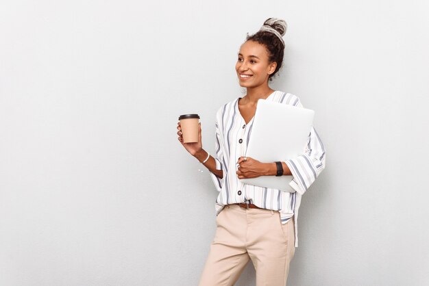 Portrait of cheerful african business woman with dreads isolated on white drinking coffee holding laptop computer.