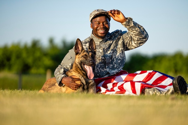 Portrait of cheerful American soldier and his military dog lying on the grass