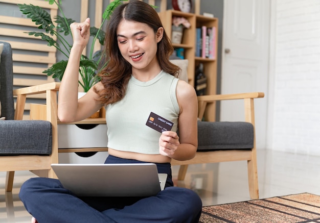 Portrait cheerful Asia girl shopping online and holding in hands demonstrating bank card at home