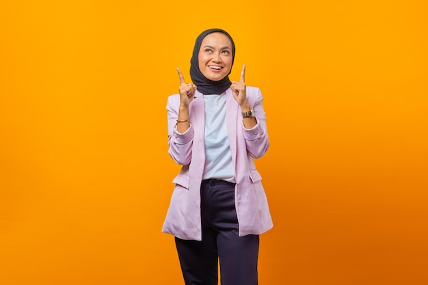 Portrait of cheerful Asian business woman pointing up. isolated yellow background