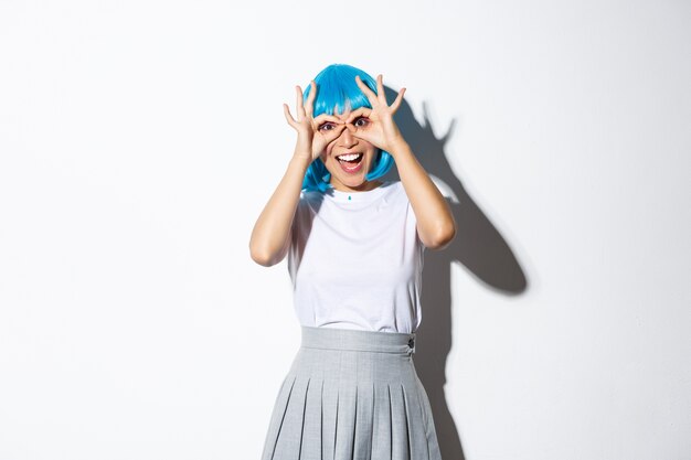 Portrait of cheerful asian girl looking amazed at camera, wearing blue wig and costume for halloween party, standing.