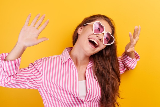 Portrait of cheerful Asian Kazakh young woman dressed casual and glasses smiling joyfully, laughing and fooling around on yellow background, girl enjoys summer holidays, vacation