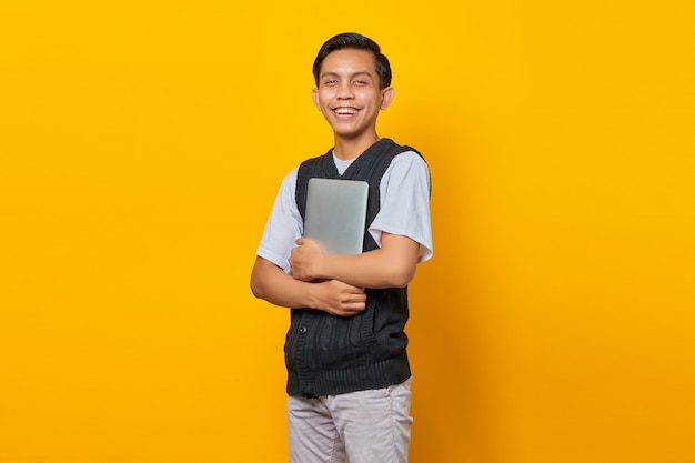 Portrait of cheerful asian man bring laptop over yellow background