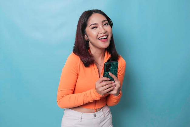 A portrait of a cheerful Asian woman looking at her smartphone over blue background